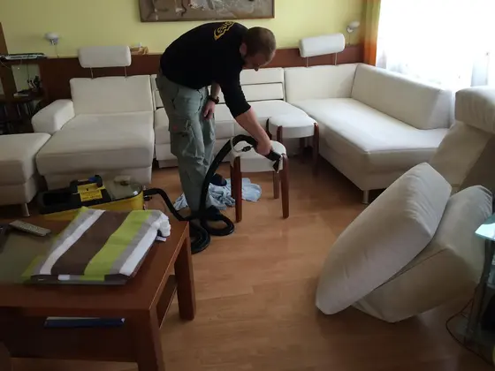 Tepovanie sedacej súpravy: technik v čiernom pri bielej rohovej súprave a stolíku s pruhovaným textilom