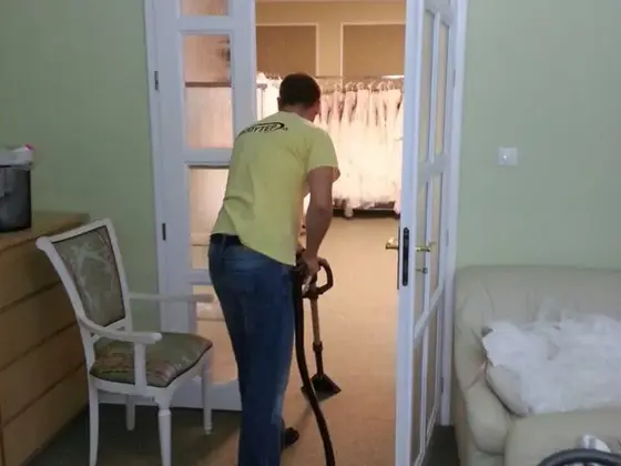 Tepovanie koberca v Bratislave: technik so strojom čistí zelenkavý koberec, v ďalšej izbe visia šaty
