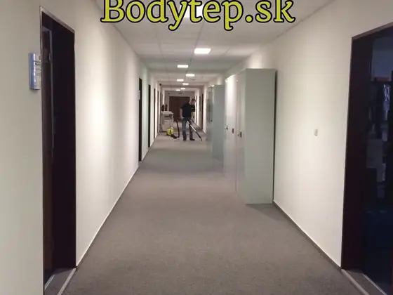 Tepovanie koberca v Bratislave: sivý koberec v dlhej kancelárskej chodbe, v diaľke technik so strojom