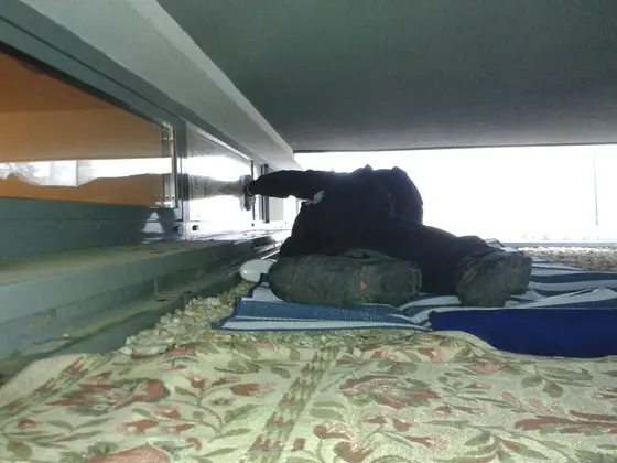 Umývanie okien v stiesnenom priestore: technik v ľahu na podložke dosiahne na okno pod previsom budovy