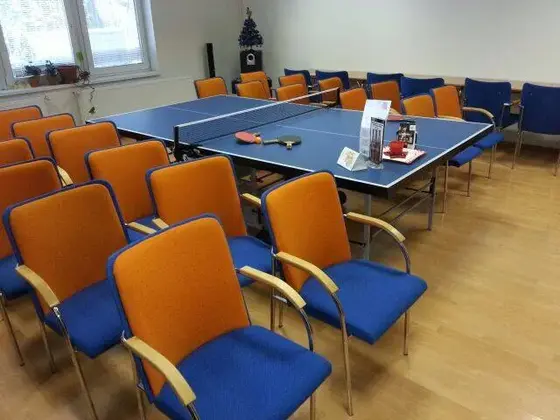 Čistenie stoličiek v spoločenskej miestnosti: oranžovo-modré stoličky okolo stola na stolný tenis