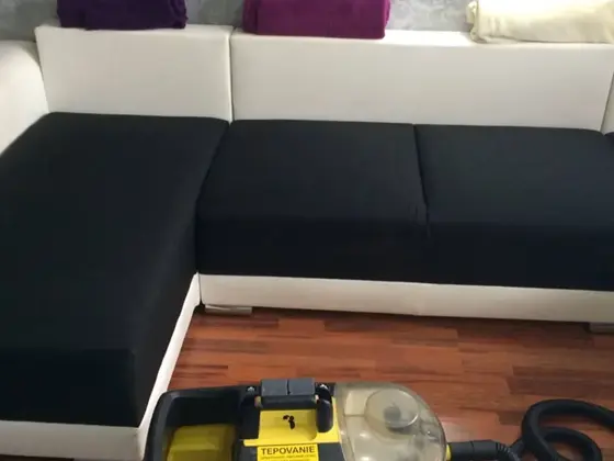 Tepovanie rohovej sedačky s čiernymi sedákmi a bielym operadlom, v popredí tepovací stroj na parketách