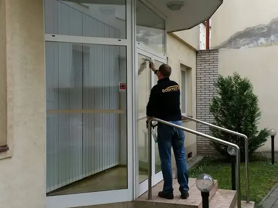 Umývanie vstupných dverí rodinného domu: technik stojí na schodoch a čistí sklenené dvere, vedľa zábradlie a ker