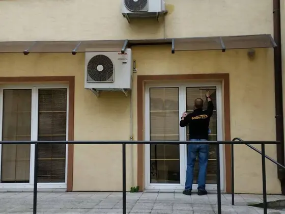 Umývanie okien v Bratislave: technik čistí presklené dvere terasy na žltej fasáde, nad nimi visí klimatizácia