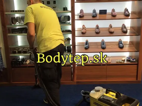 Tepovanie koberca v Bratislave: technik v žltom tričku pracuje na modrom koberci v predajni obuvi pri regáloch