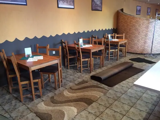 Tepovanie kobercov v reštaurácii, zrolovaný hnedý koberec pri stoloch a vlnitý béžovohnedý koberec na dlaždiciach