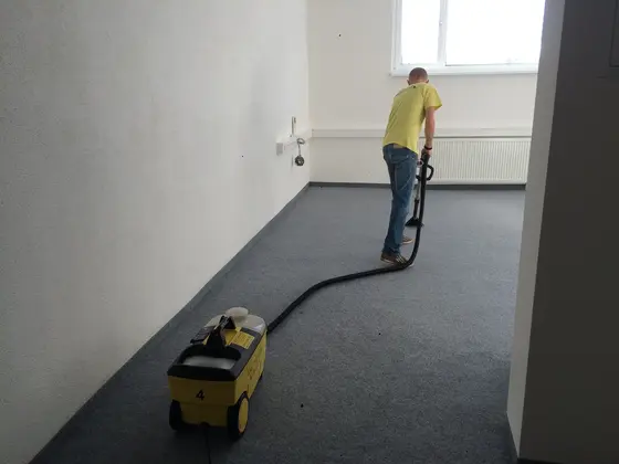 Tepovanie koberca v prázdnej kancelárii v Bratislave, pracovník v žltom tričku a stroj s číslom 4 na sivomodrom koberci