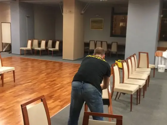 Tepovanie stoličiek v spoločenskej sále v Bratislave, pracovník sa skláňa nad radom stoličiek s krémovým čalúnením