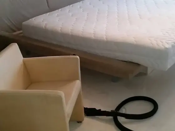 Tepovanie postele a čistenie matraca v spálni, biely prešívaný matrac, béžové kreslo a čierna hadica na koberci
