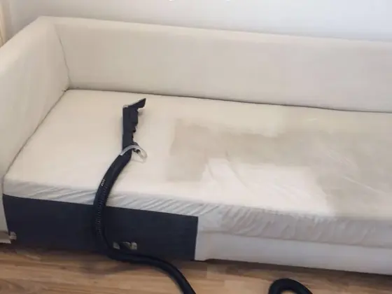 Čistenie čalúneného nábytku, biela sedačka s tmavou doskou na boku a hadicou položenou cez sedák