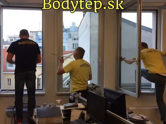 Umývanie okien v kancelárii v Bratislave, traja pracovníci zvnútra čistia okná s výhľadom na strechy