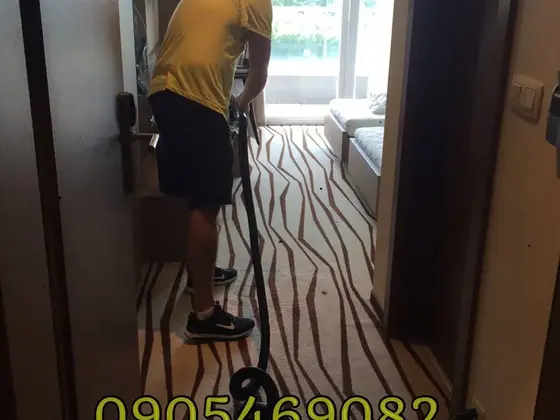 Tepovanie celoplošného koberca na chodbe hotelovej izby, pracovník pri vchode s hadicou