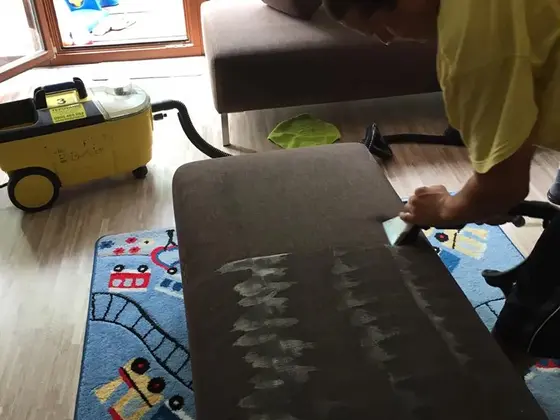Tepovanie gauča s hnedým čalúnením v detskej izbe, pracovník ťahá hubicu po sedáku