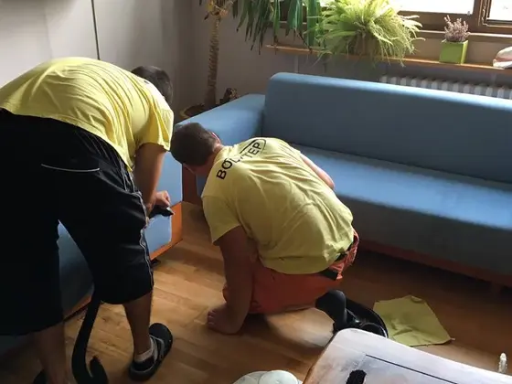Tepovanie sedacej súpravy v modrej látke v Bratislave, dvaja pracovníci v obývačke s rastlinami