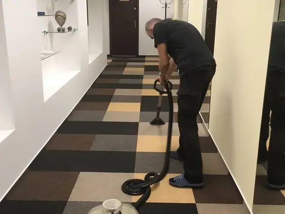 Tepovanie kobercových štvorcov na chodbe kancelárie v Bratislave, pracovník so strojom na hadici