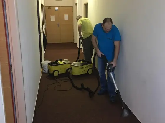 Tepovanie koberca na chodbe: dvaja muži s dvoma žltými tepovačmi na hnedom koberci v Bratislave