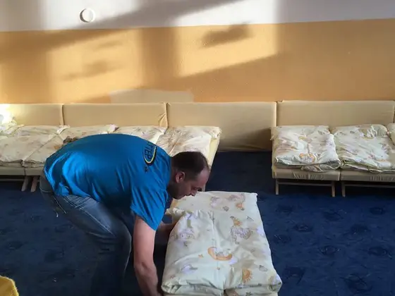 Tepovanie koberca: muž v modrom tričku odsúva lehátko s paplónom na tmavomodrom koberci v miestnosti