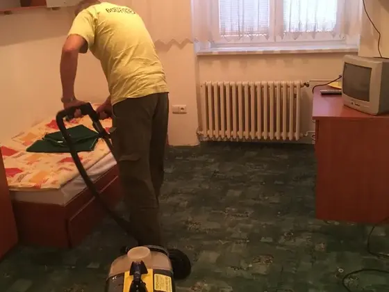Tepovanie koberca v Bratislave: muž s tepovačom v izbe so zeleným vzorovaným kobercom, posteľ a písací stôl