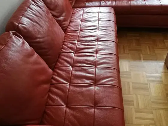 Ošetrenie kože na sedačke: červenohnedá rohová sedačka z kože s prešívaním a parketovou podlahou
