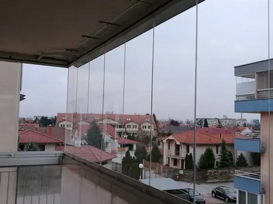 Umývanie okien na zasklenom balkóne: priehľadné sklá s výhľadom na rodinné domy a ulicu