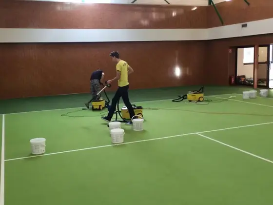 Tepovanie kobercov v Bratislave: pracovník s tepovačom na zelenej ploche haly, okolo biele vedrá