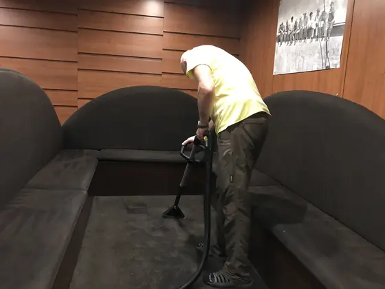 Tepovanie čalúnených lavíc: technik s hubicou medzi tmavými sedákmi so zaoblenými operadlami