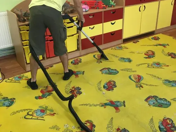 Tepovanie detského koberca: žltý koberec s autíčkami a technik s hubicou pri regáloch