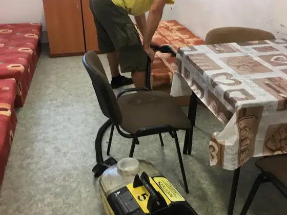 Tepovanie kancelárskej stoličky: žltý tepovací stroj pri stole s obrusom v izbe s posteľami