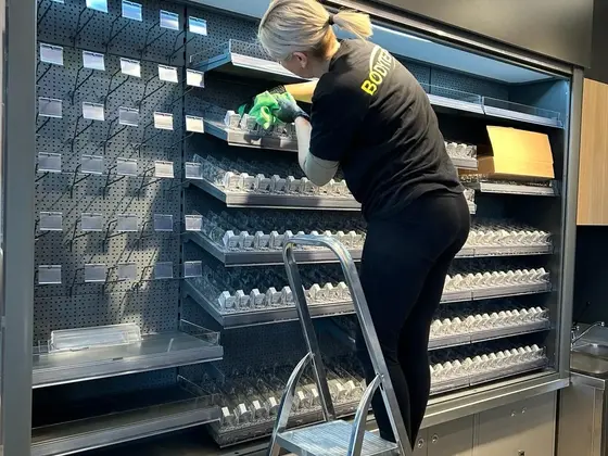 Upratovanie obchodu: utieranie vysokého regálu z rebríka pri sklenených policiach