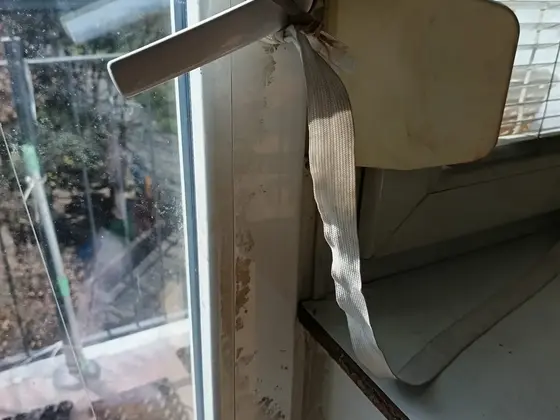 Čistenie okna: zašpinený rám a parapet pri okennej rukoväti pred čistením, za oknom balkón