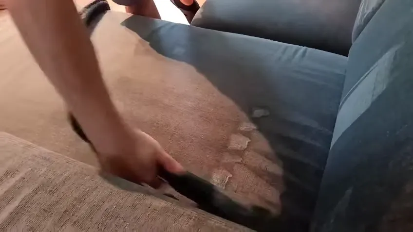 Video: pracovník tepuje béžový gauč s modrými vankúšmi ručnou hubicou