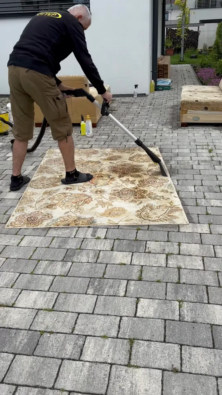 Video: pracovník tepuje podlahovou hubicou kusový koberec s kvetovaným vzorom na dlažbe