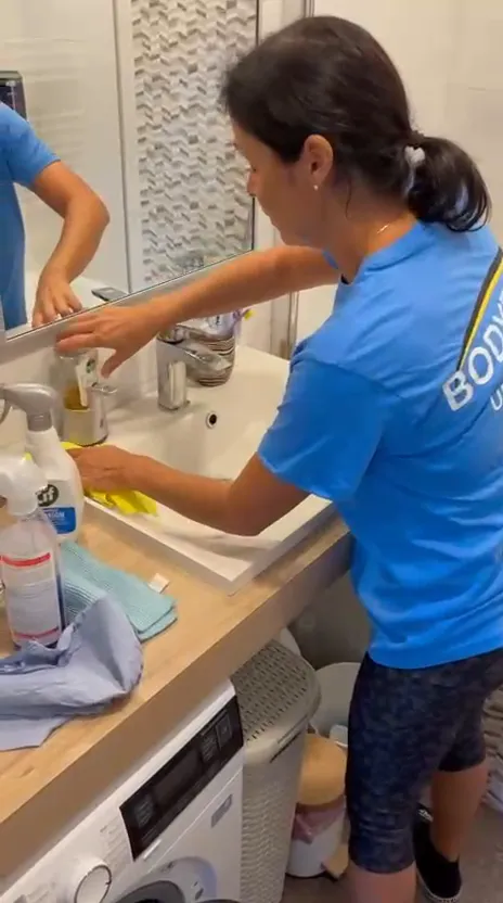 Video: pracovníčka v tričku BODYTEP utiera žltou handrou umývadlo a batériu v kúpeľni