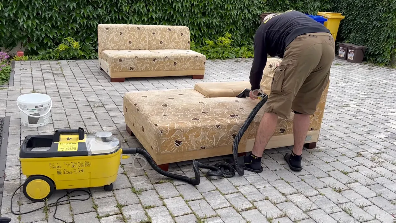 Video: pracovník tepuje sedaciu súpravu s kvetovaným poťahom vonku na dlažbe, vedľa stojí žltý tepovač